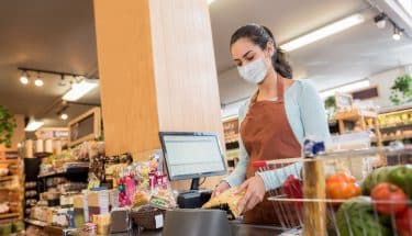 Cashier working at the supermarket wearing a facemask while scanning products